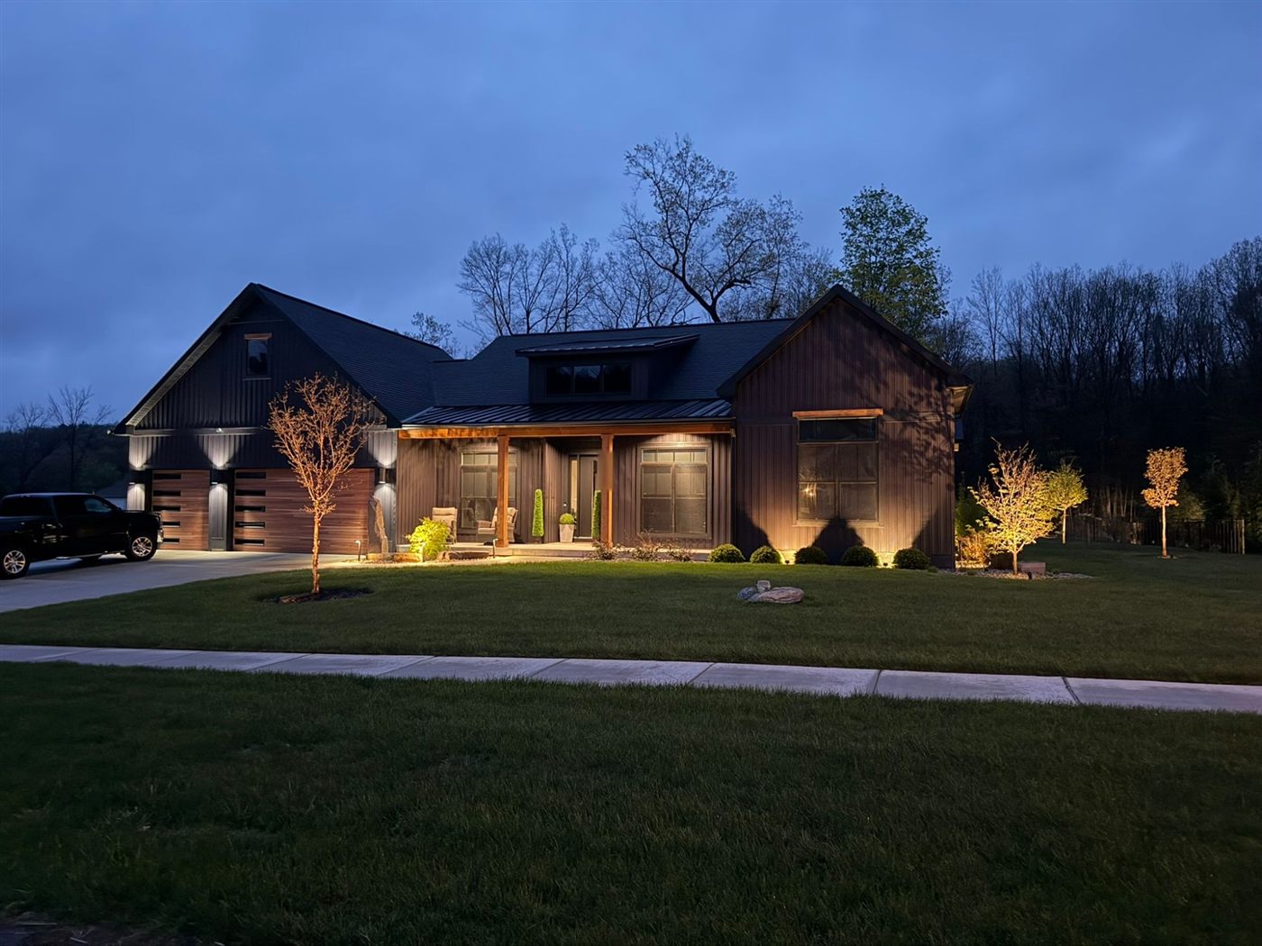 Modern home at dusk with landscape lighting on the trees, entry, and beds