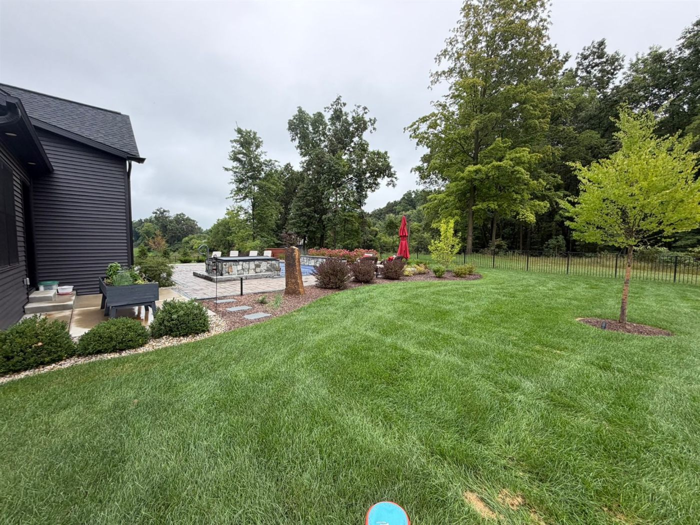 Backyard with paver patio, stone fire feature, planting beds, and new trees