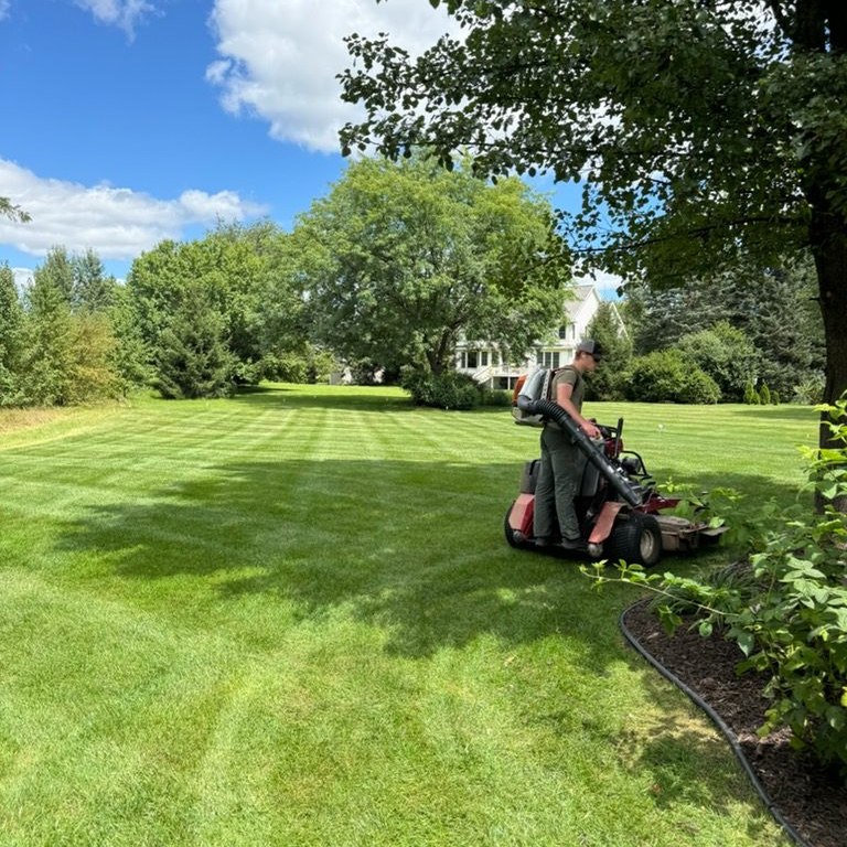 Jepson Landscaping team member mowing on a stand-on mower while wearing a backpack blower