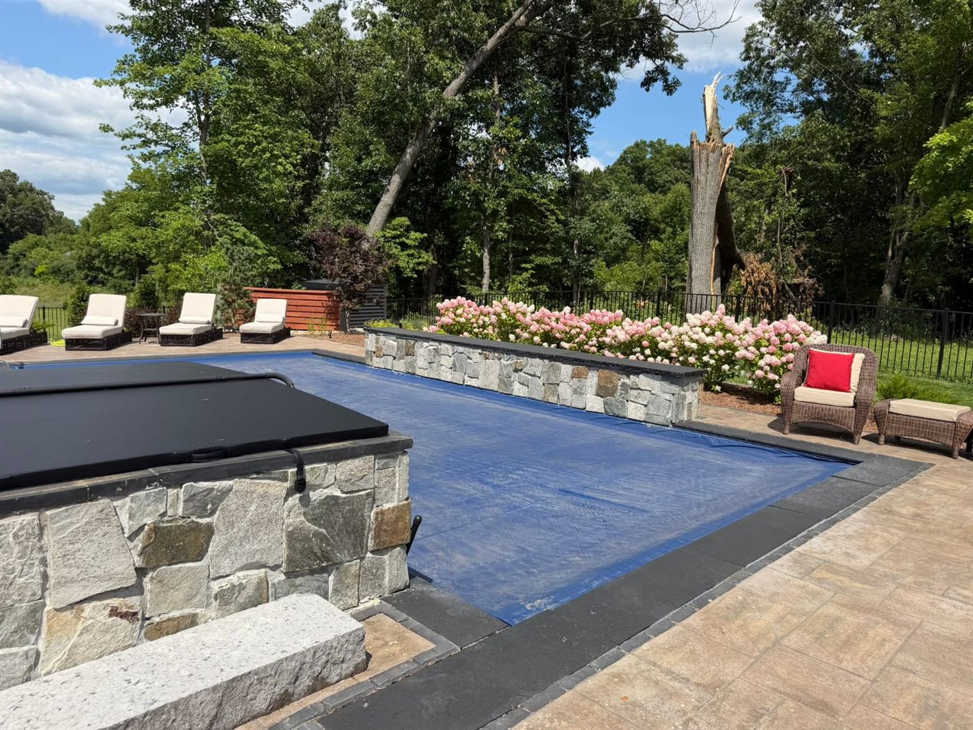 Pool and hot tub with stone walls, hydrangeas, and paver patio