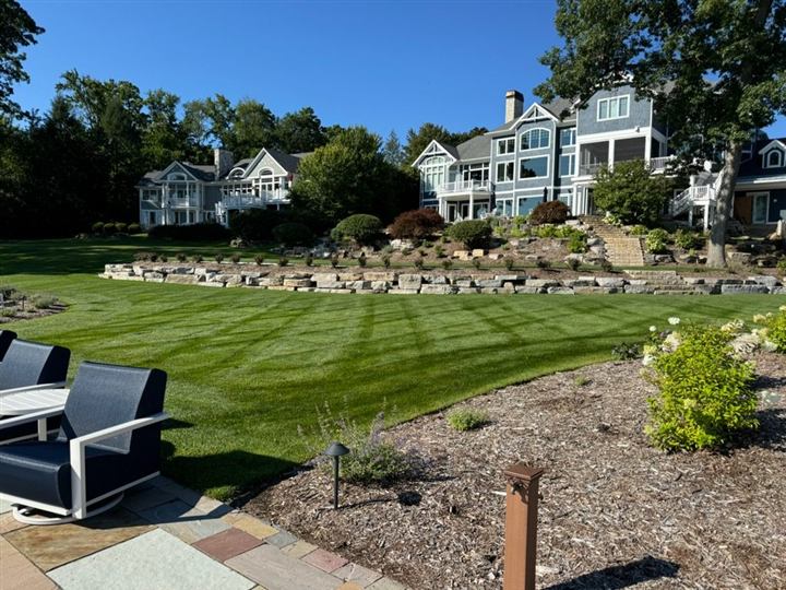 Striped lawn and stone retaining wall in front of a blue lakefront home